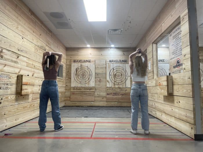 two women throwing axes at a wooden indoor target